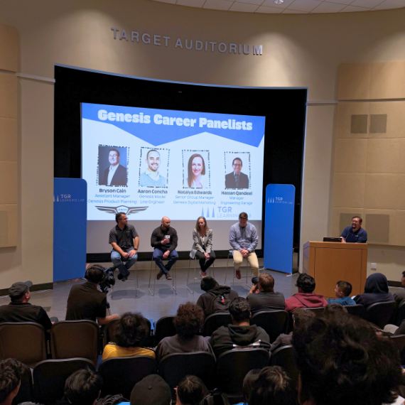Panel discussion on stage at Target Auditorium; five speakers seated; large screen reads 'Genesis Career Panelists' with speaker photos.