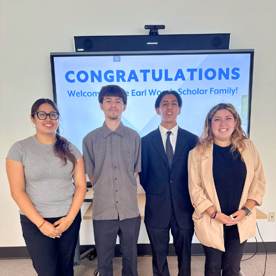 Four students pose in front of a screen reading 'CONGRATULATIONS' and 'Welcome ... Scholar Family', celebrating a scholarship.