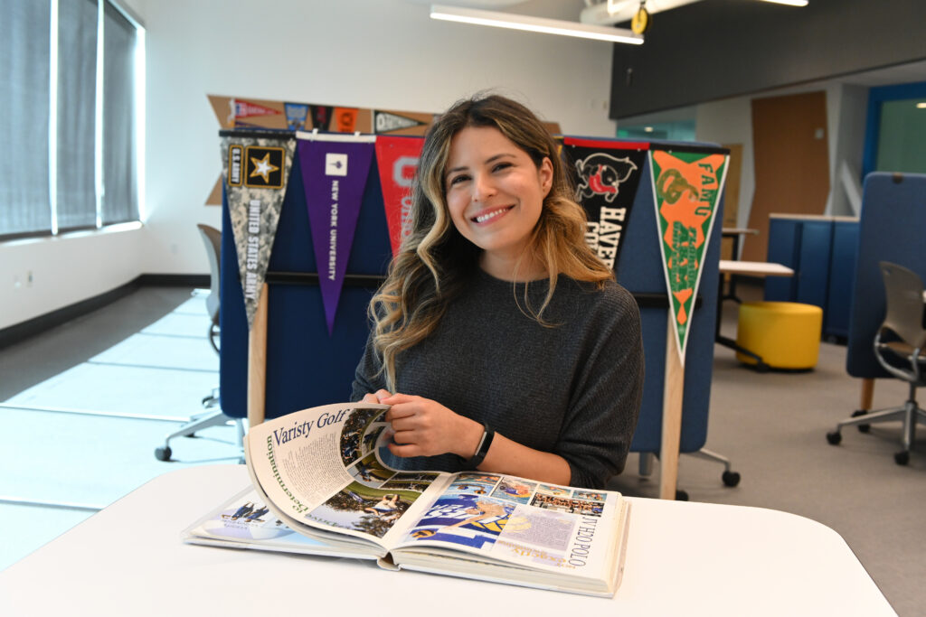 Woman smiling while reading a magazine at a white table in a bright room with pennant banners in the background
