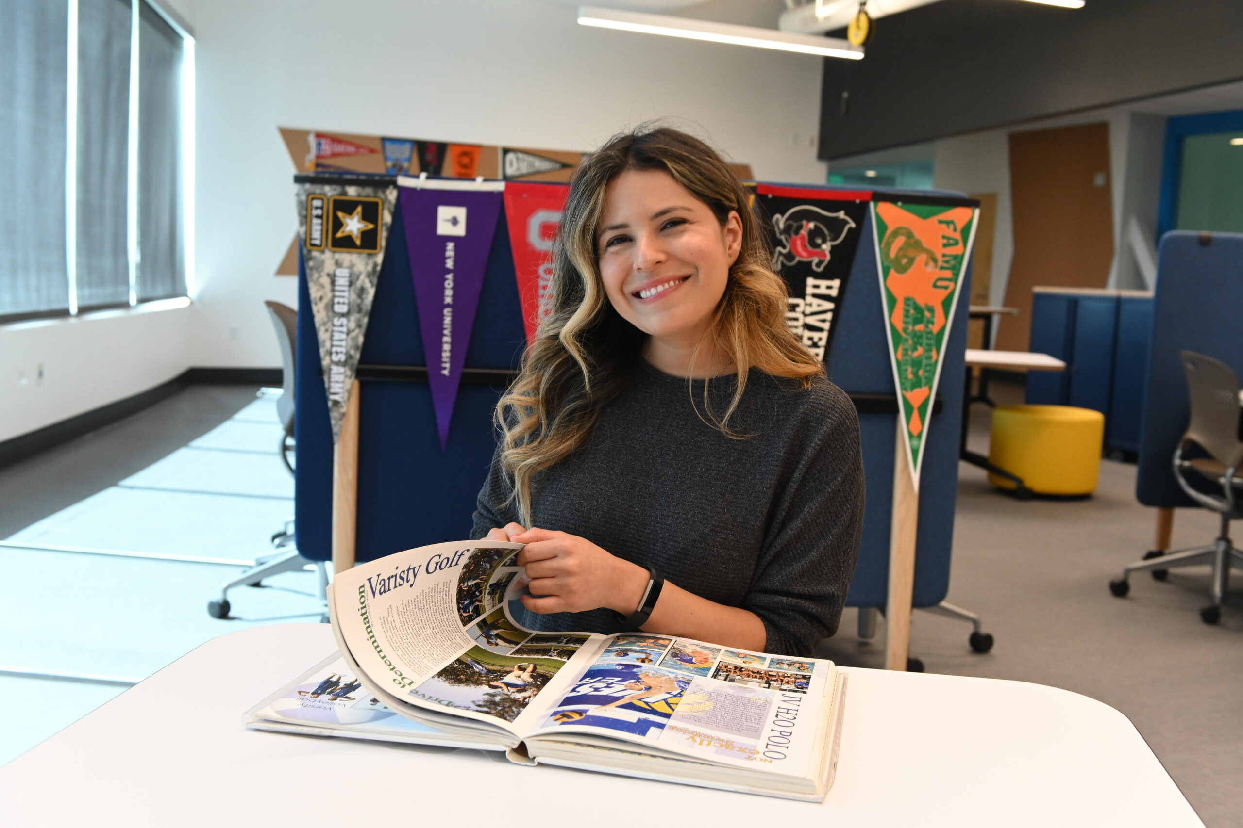 Woman smiling while reading a magazine at a white table in a bright room with pennant banners in the background