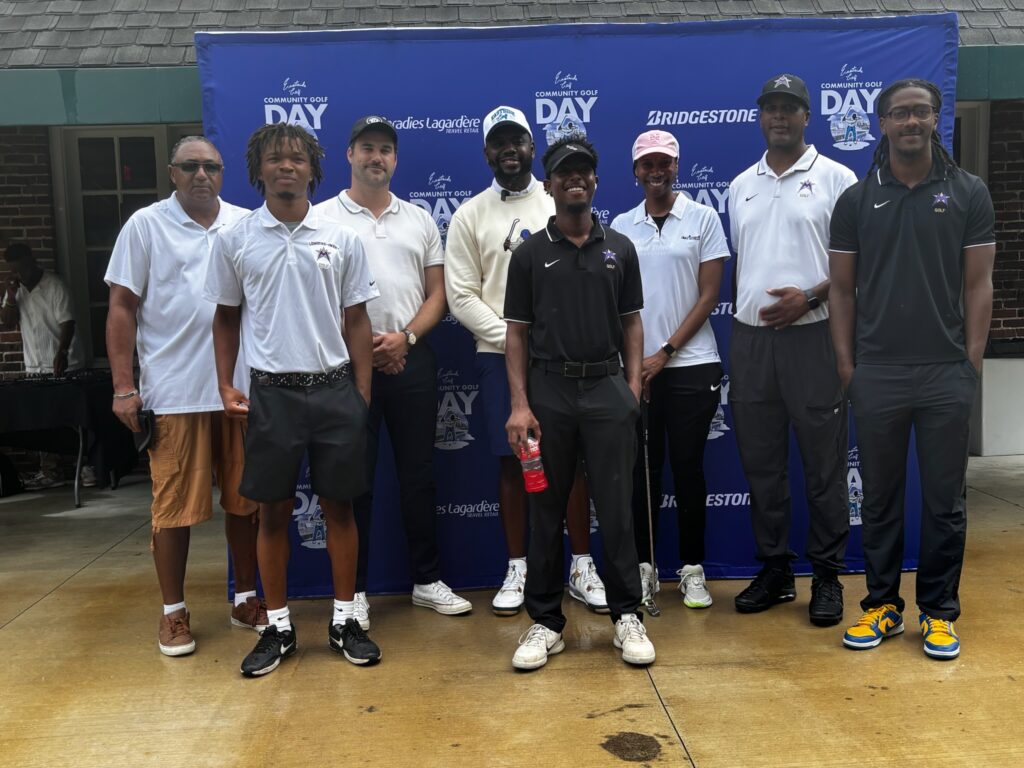 Eight male golfers posing together in front of a blue 'Community Golf Day' backdrop, smiling at the camera.