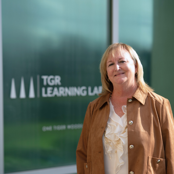 Woman smiling in front of a glass wall with 'TGR Learning Lab' logo outside a building.