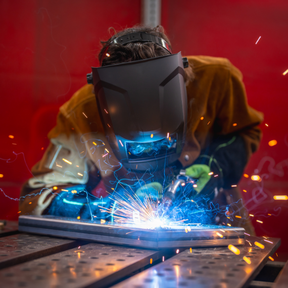 Welder in a protective helmet and gloves welding metal with bright sparks flying.