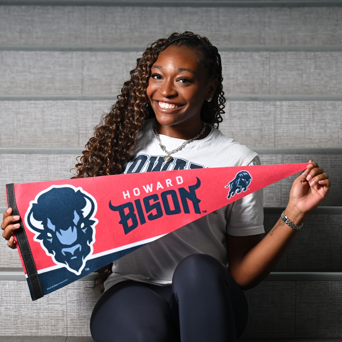 Smiling woman sitting and holding a red Howard Bison pennant with a blue bison logo.