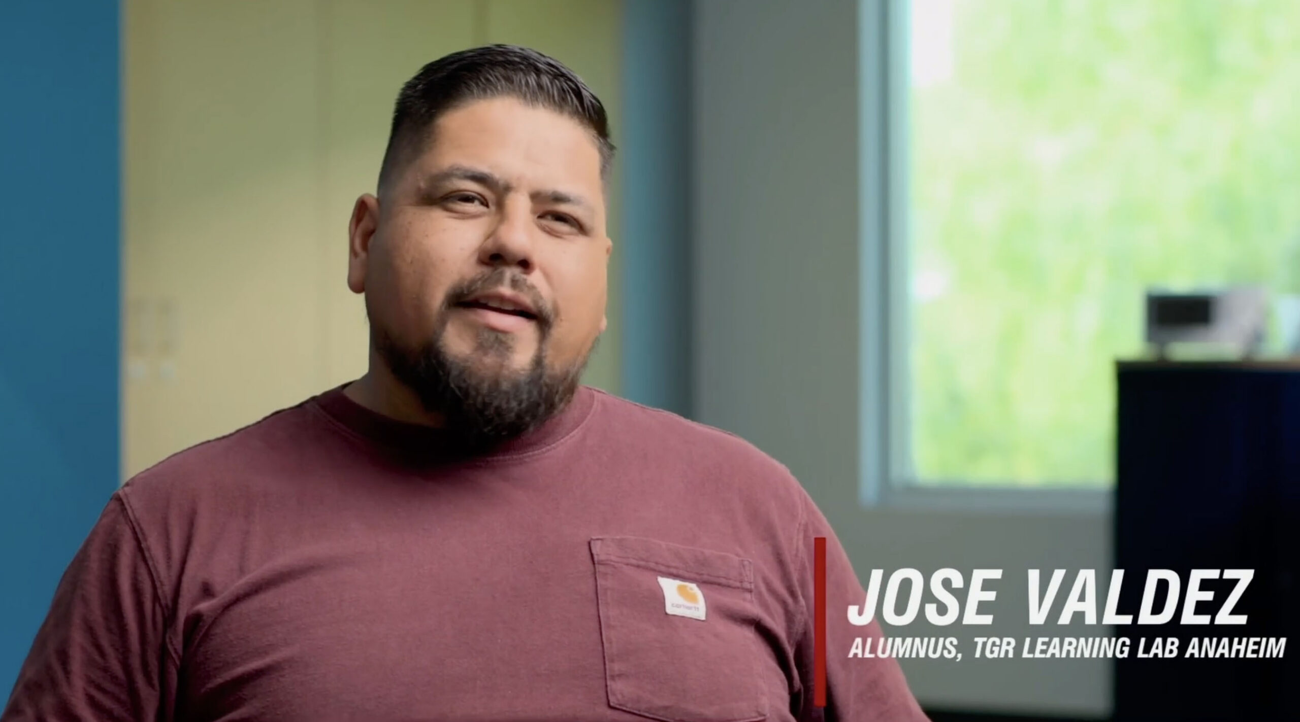 Video still of a man with short dark hair and a beard wearing a maroon t-shirt, in a bright room; on-screen text shows the name 'JOSE VALDEZ' (and role text partially visible).