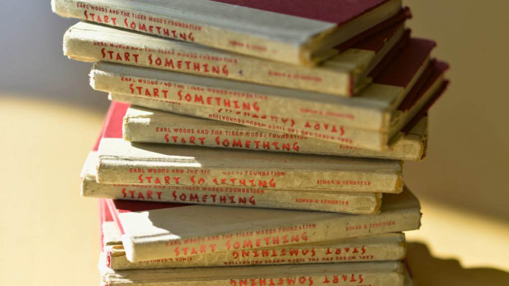 Stack of old books with red 'START SOMETHING' text on spines, warm lighting in a cozy room