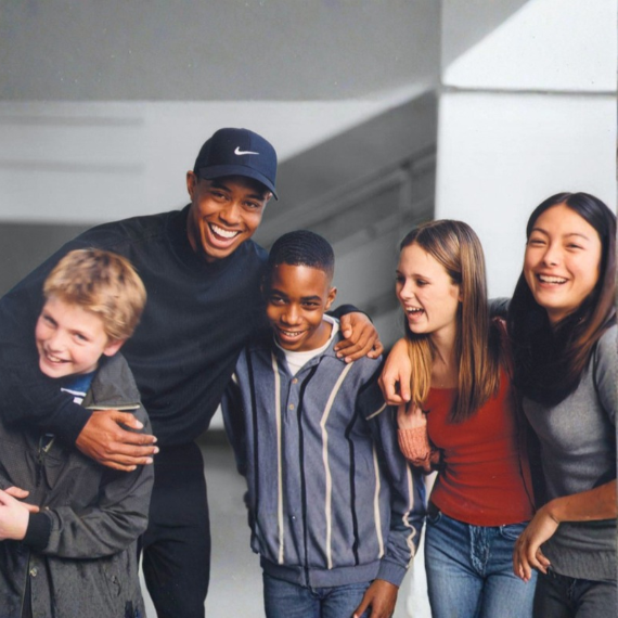 A cheerful group of five young people standing arm-in-arm with a smiling coach in a hallway.