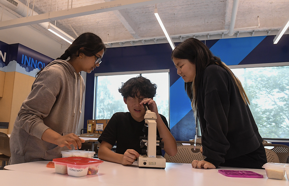 students working on a microscope in STEM at the TGR Learning Lab after school programs.